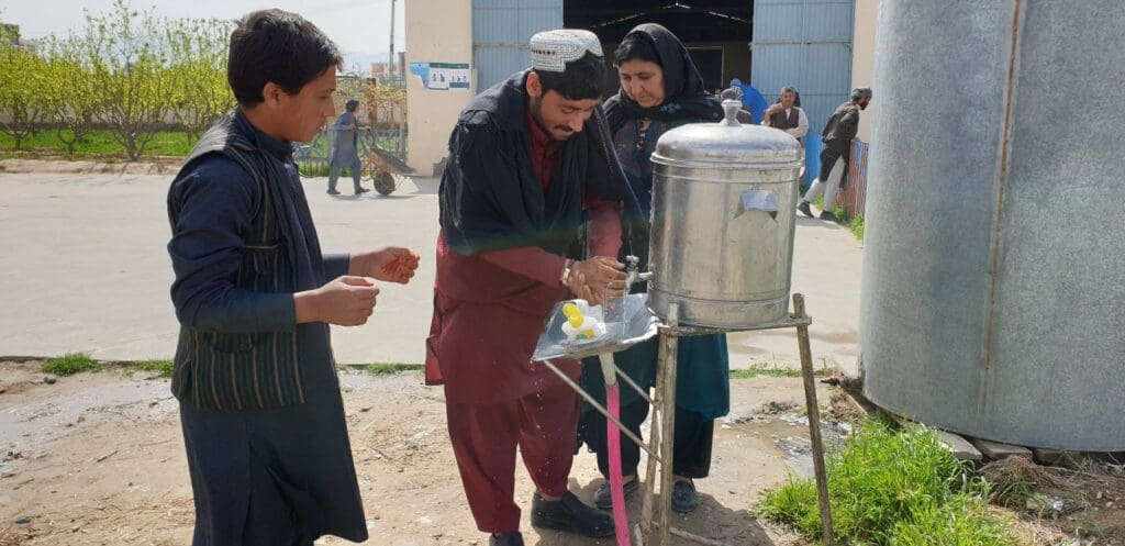 Three Afghans wash their hands at a sanitizing station outside a food distribution center. 