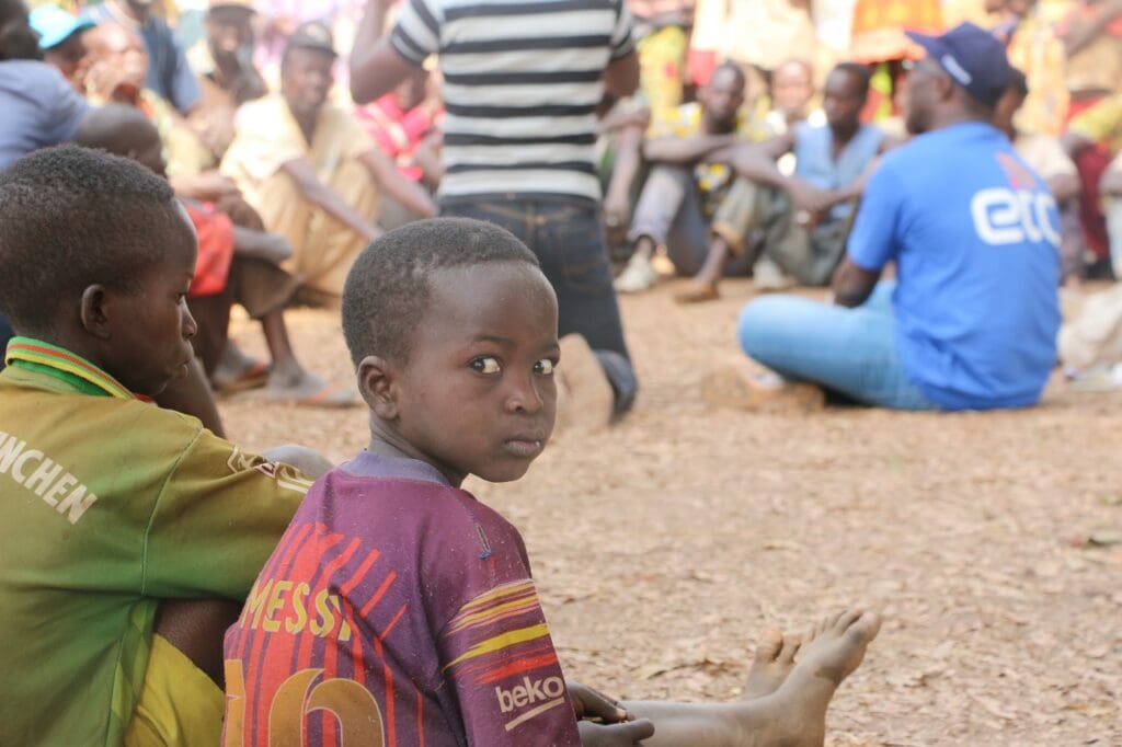 Children pictured sitting on the ground at a community meeeting