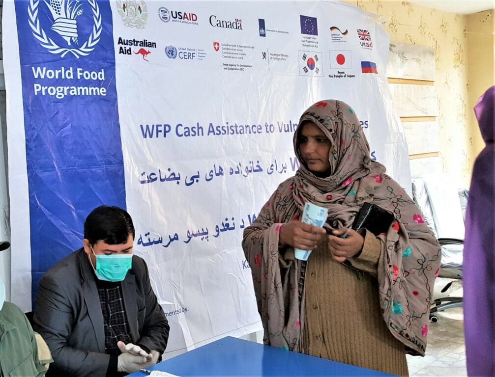 A WFP worker in a mask registers a standing woman for cash assistance.