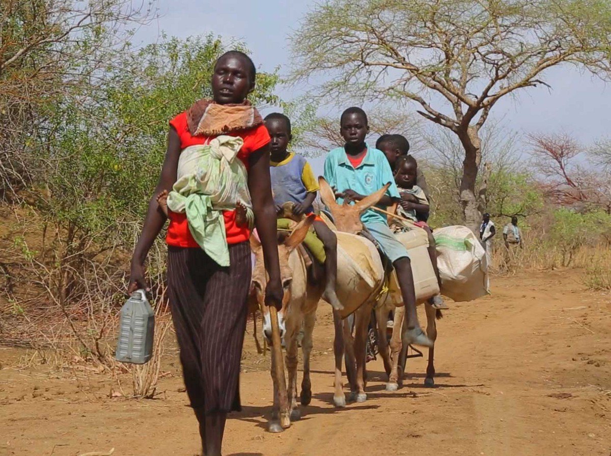 Apu Riang's family walk in a line through the South Sudanese bush
