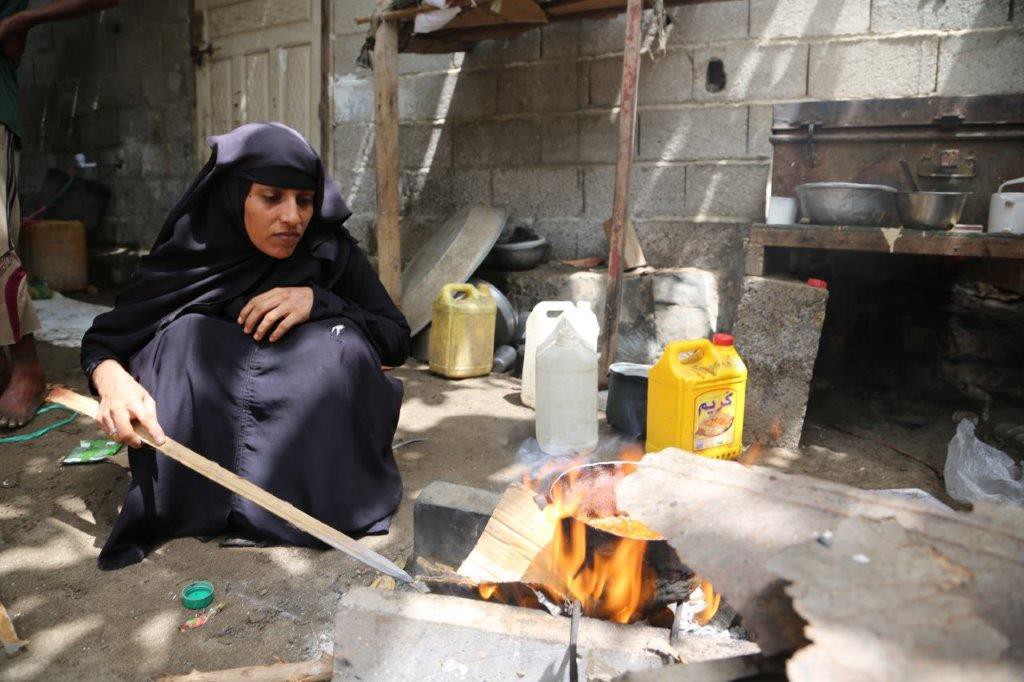 Aisha in her black hijab kneels on the ground to light up a makeshift stove using cardboard