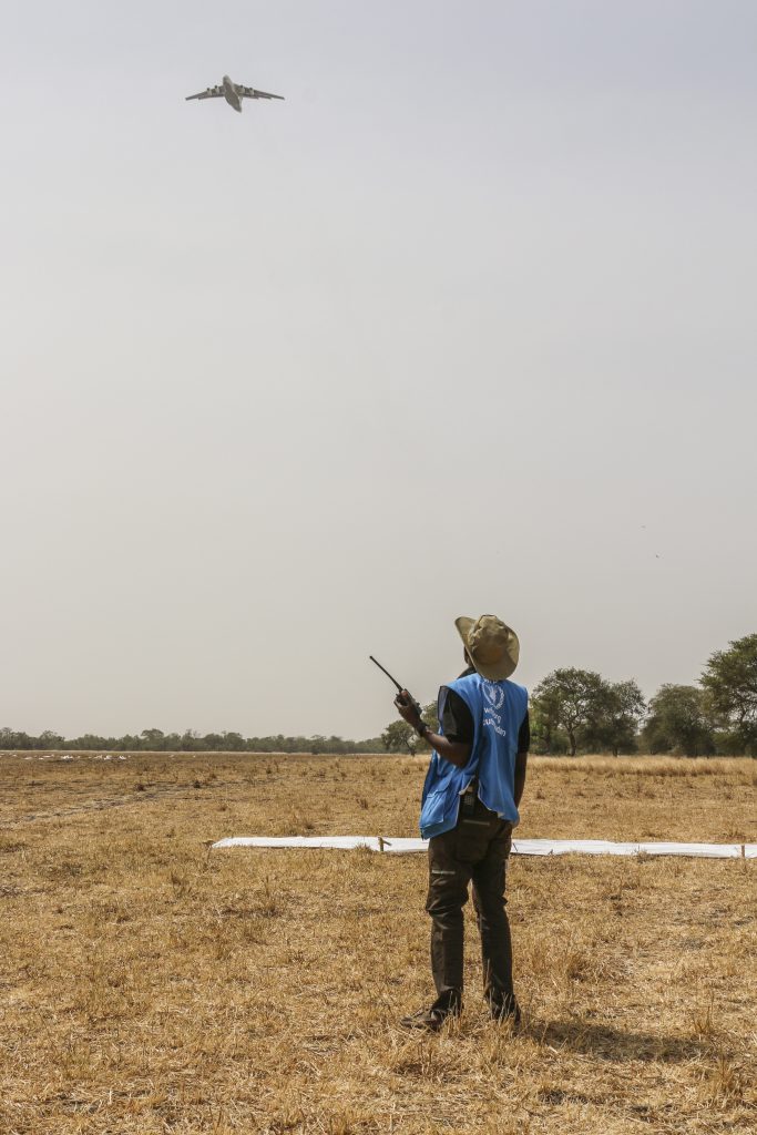 WFP Drop Zone Coordinator, Hezron Kabburu, observes the approach of an Ilyushin-76, which is about to drop bags of cereal in Thaker, Mayendit County of South Sudan. 