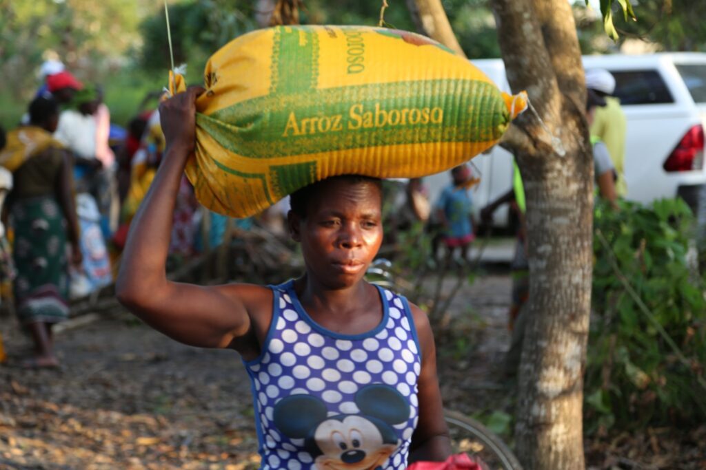A woman carries a sack of food on her head.