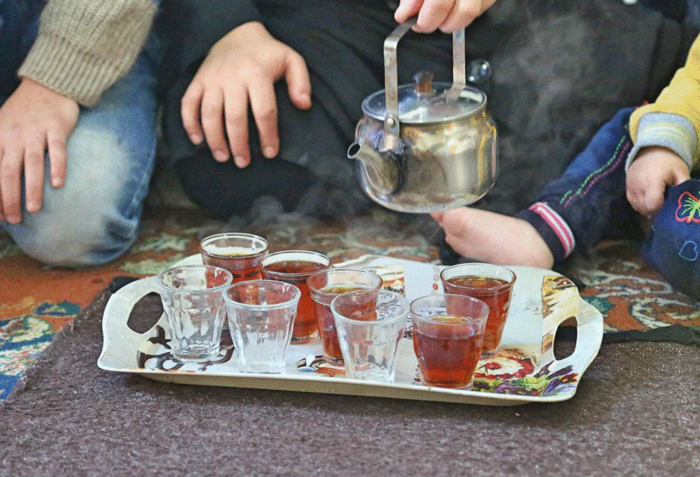 Hands are pictured holding a tea pot, pouring into a set of tea glasses