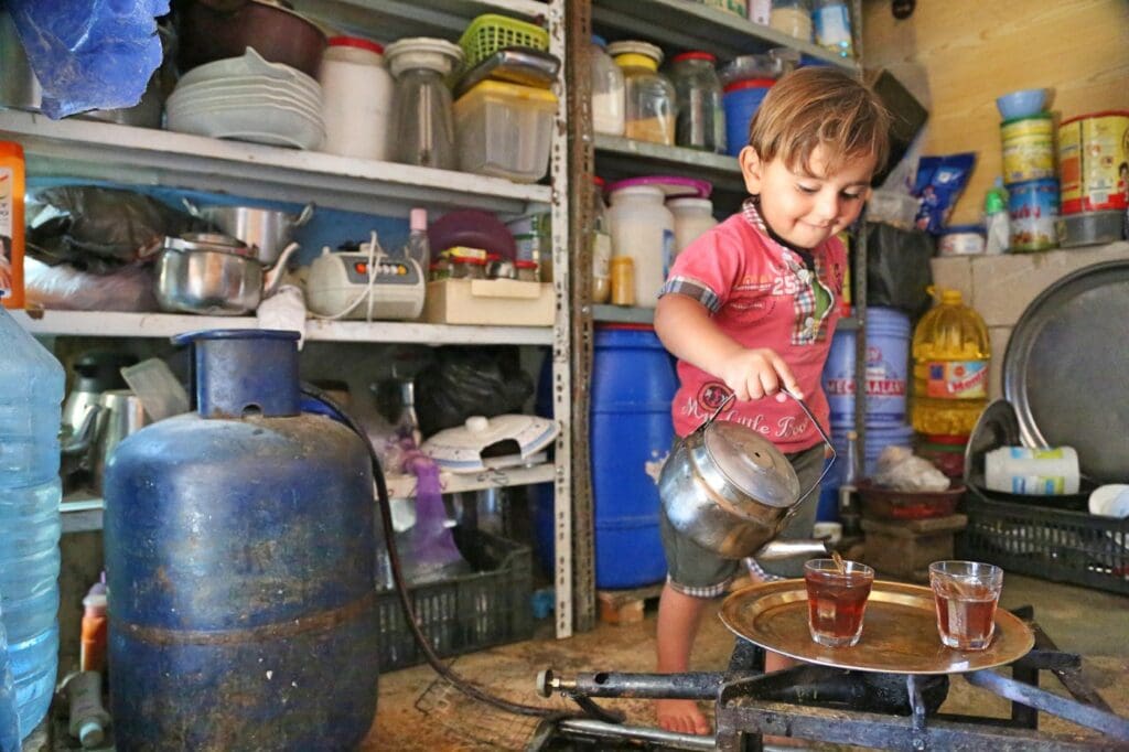 A young boy smiles while pouring a cup of tea
