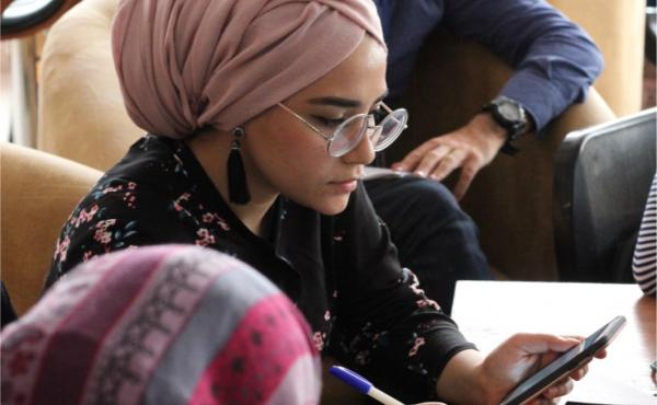 A woman in a headwrap looks down at her phone.