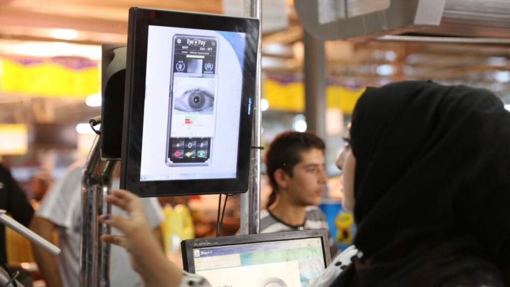 A woman in a headwrap looks into an eye scanning screen.