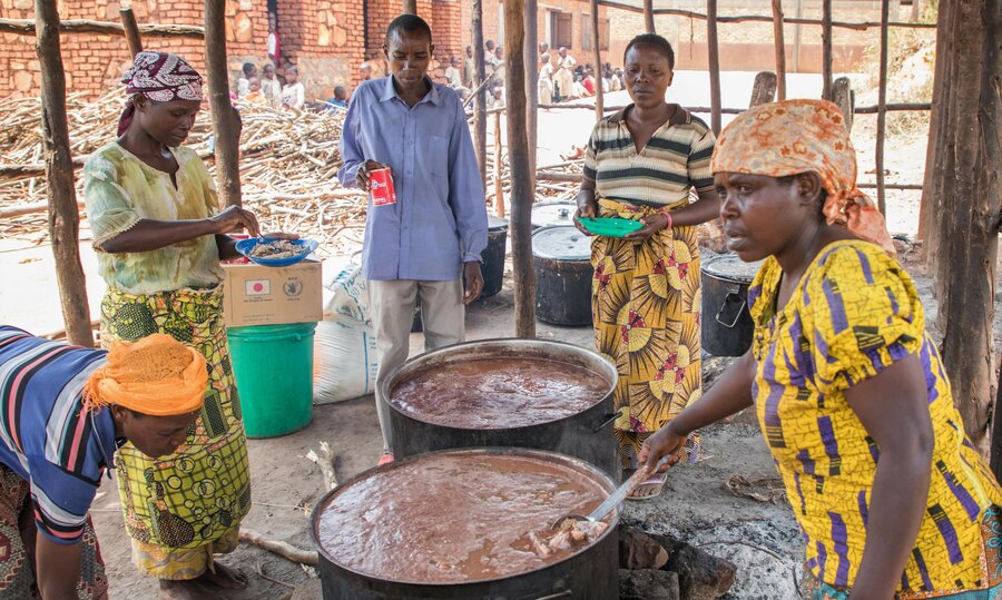 men and women cooking around large pots