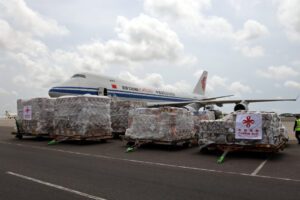 A large cargo plane sits on the tarmac in front of pallets of supplies waiting to be loaded.