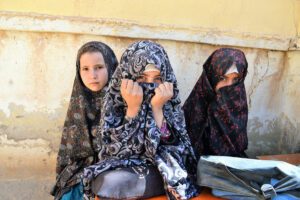 Three school girls in head wraps are seated, looking at the camera