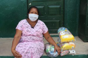 A woman in a mask and pink dress sits beside a take-home ration of food.