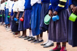 Students lined up, seen from the waist down, holding bowls and cups in their hands