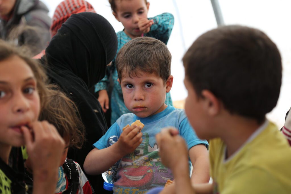 A young boy eats a biscuit, surrounded by his family.