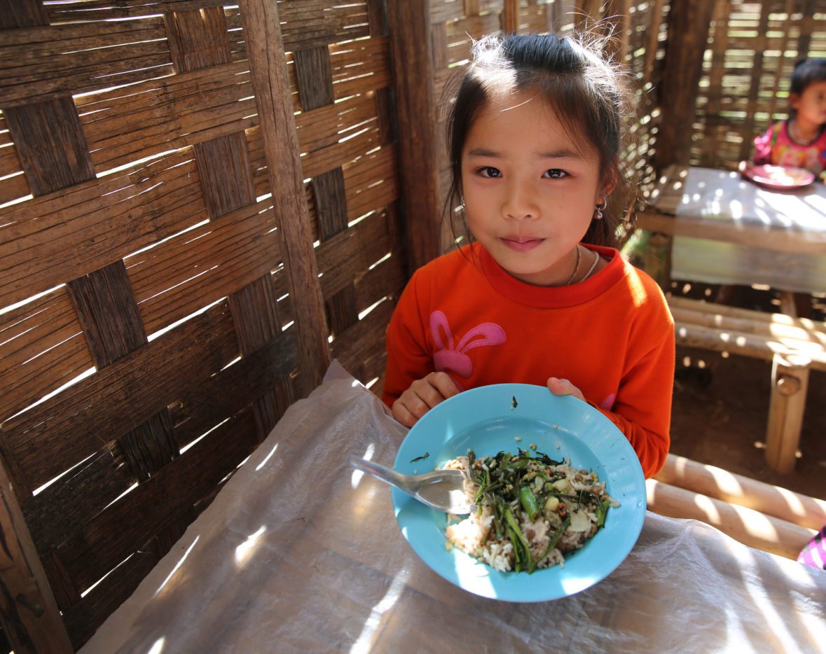 A young girl holds a bowl of food up to the camera.