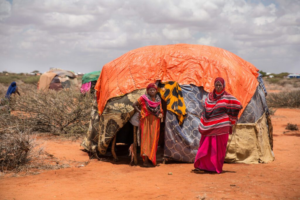 A woman stands in front of her shelter with her family at a refugee camp in Somalia.
