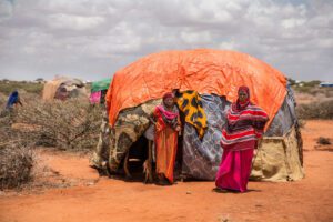 A woman stands in front of her shelter with her family at a refugee camp in Somalia.