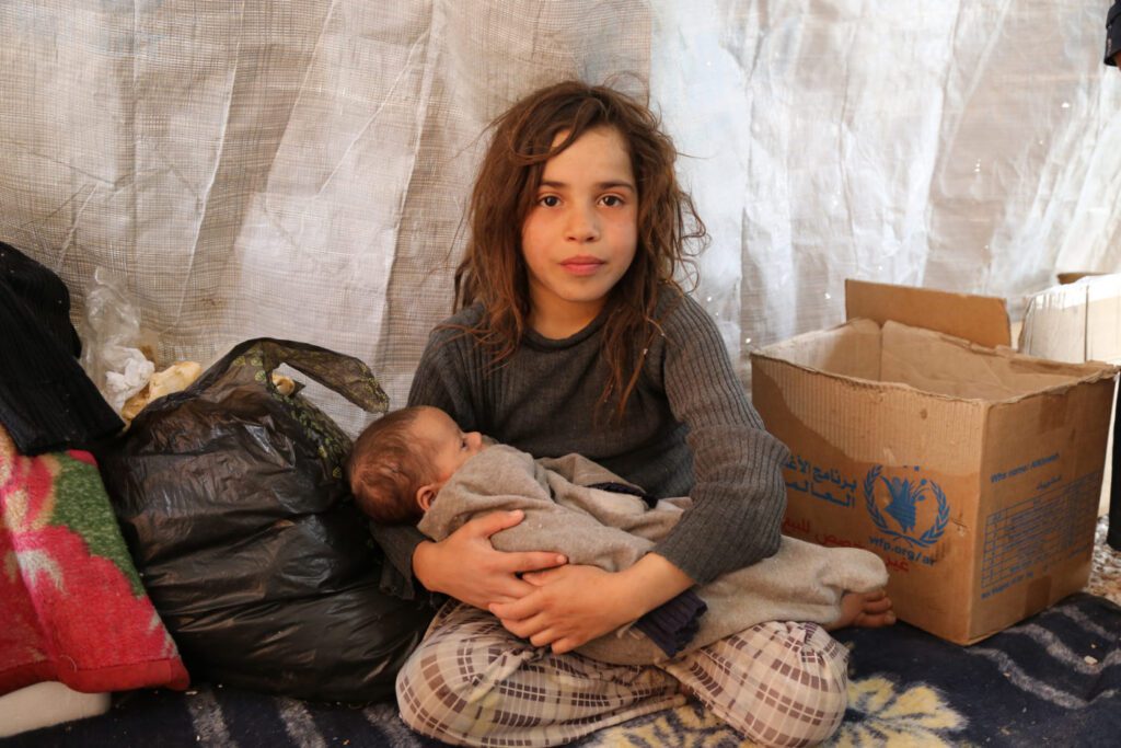 Maysa holds her 3-month-old baby sister Nada in a makeshift shelter in Syria