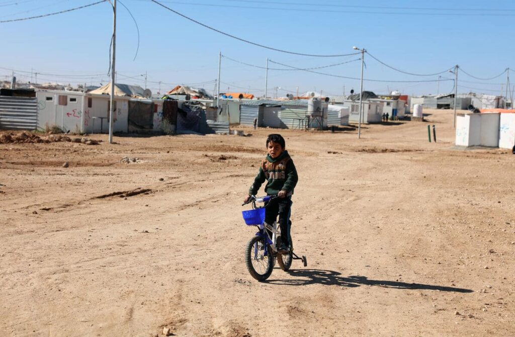 boy riding bicycle on dusty road in refugee camp