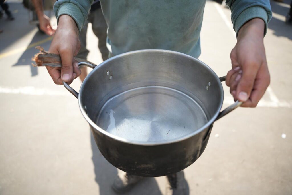 In Gaza, child holds saucepan filled with little water