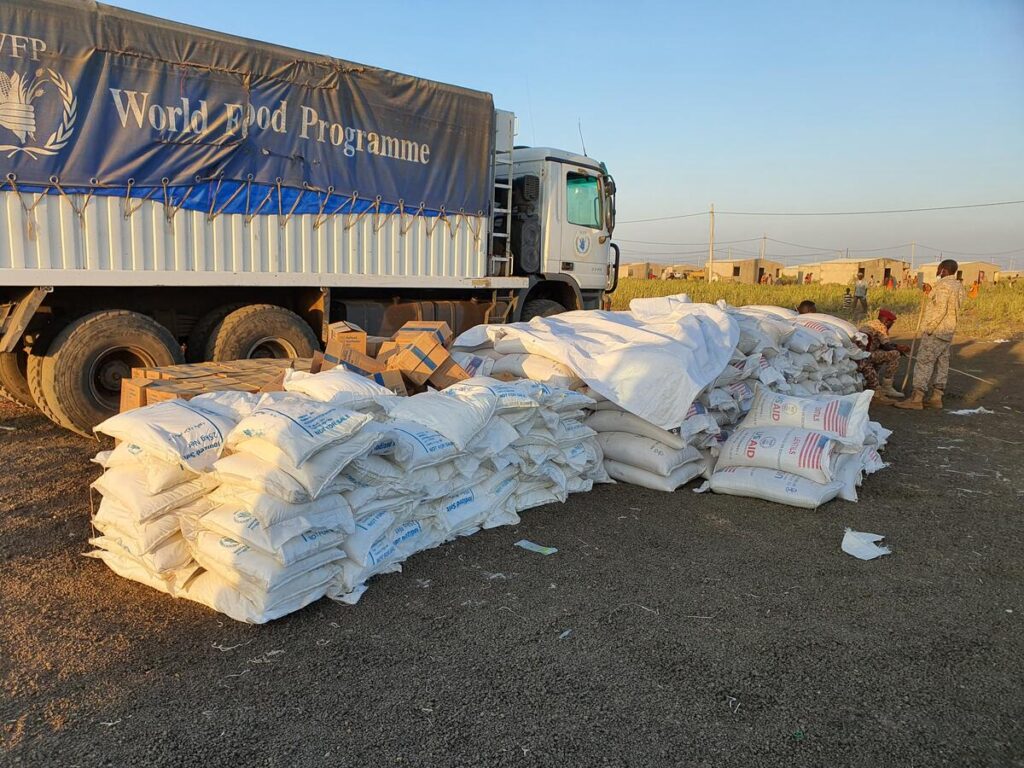 A WFP truck is parked in front of a delivery of bags of food.