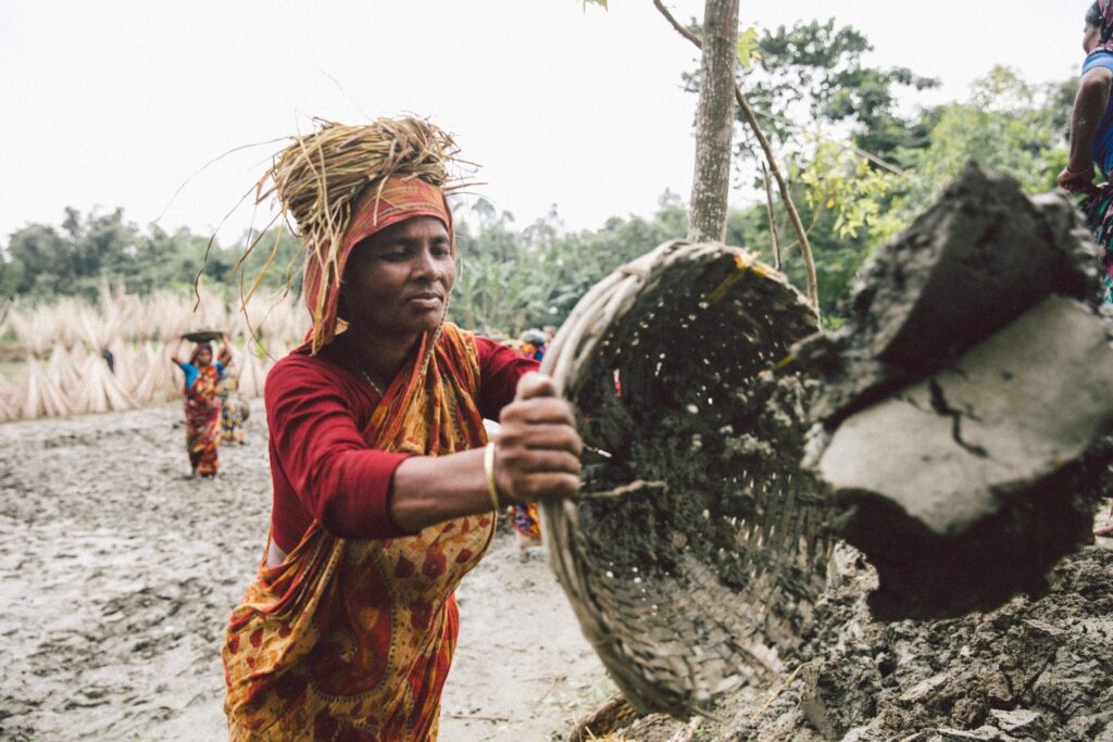A woman places a pile of dirt and mud from a basket onto the embankment that she and other participants are raising