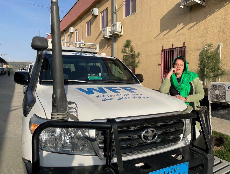 woman in green headscarf stands next to WFP truck
