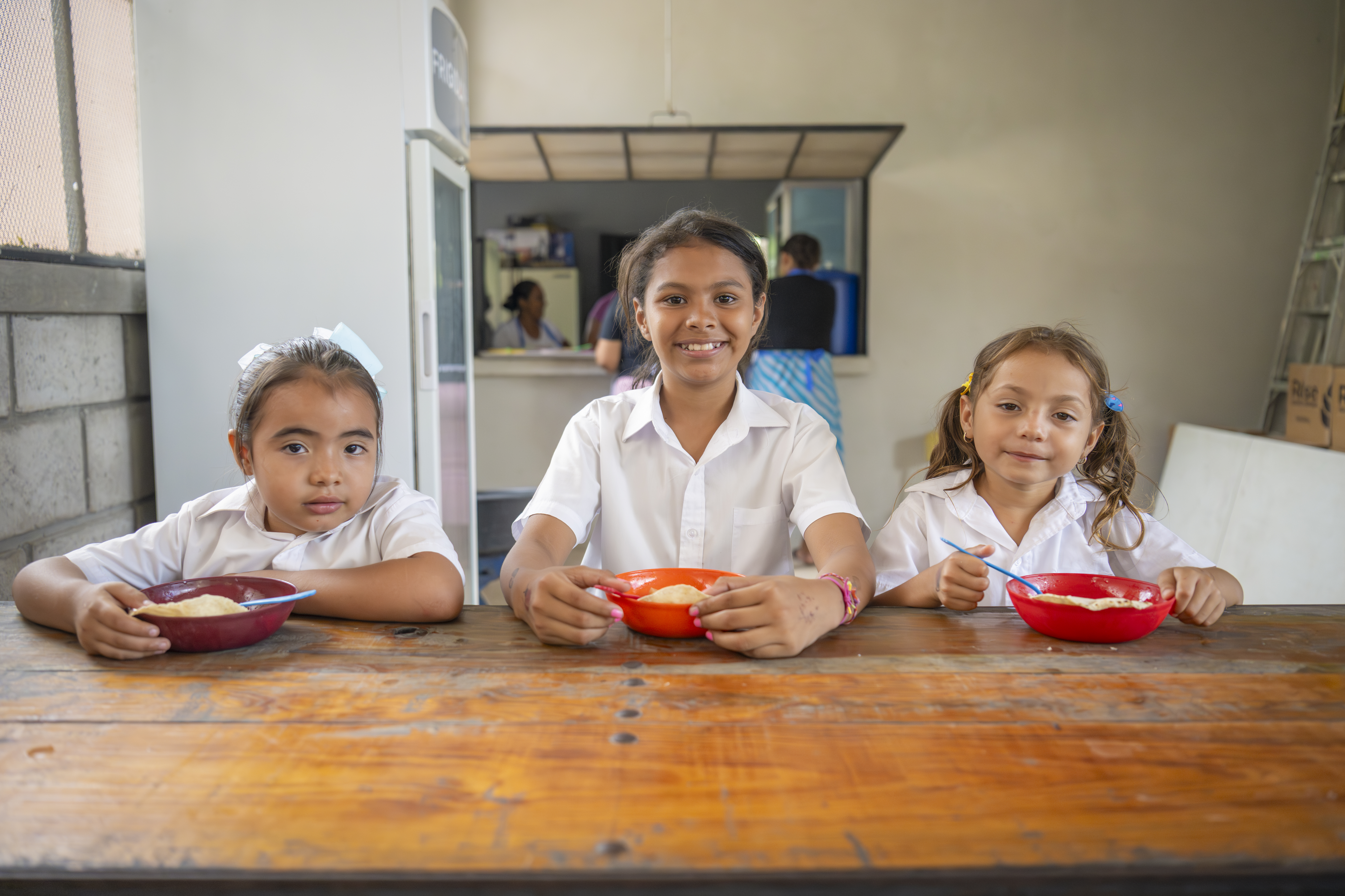 Dana, Ashly and Anyeli sit together to eat the hot school meal: red bean soup.